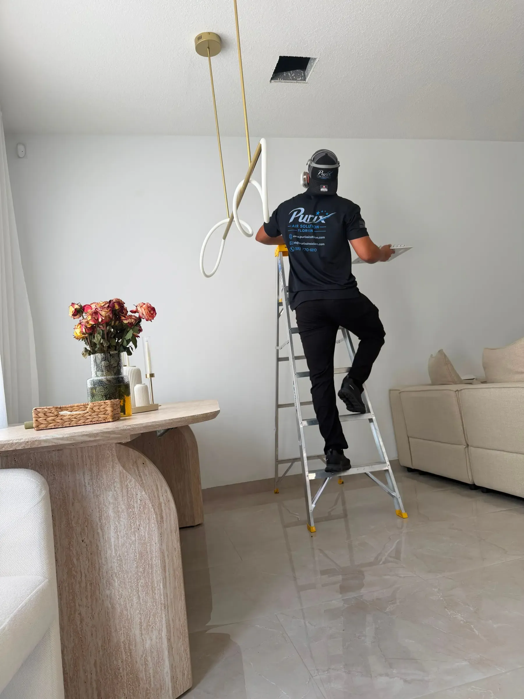 Purix technician inspecting an open ceiling vent from a ladder