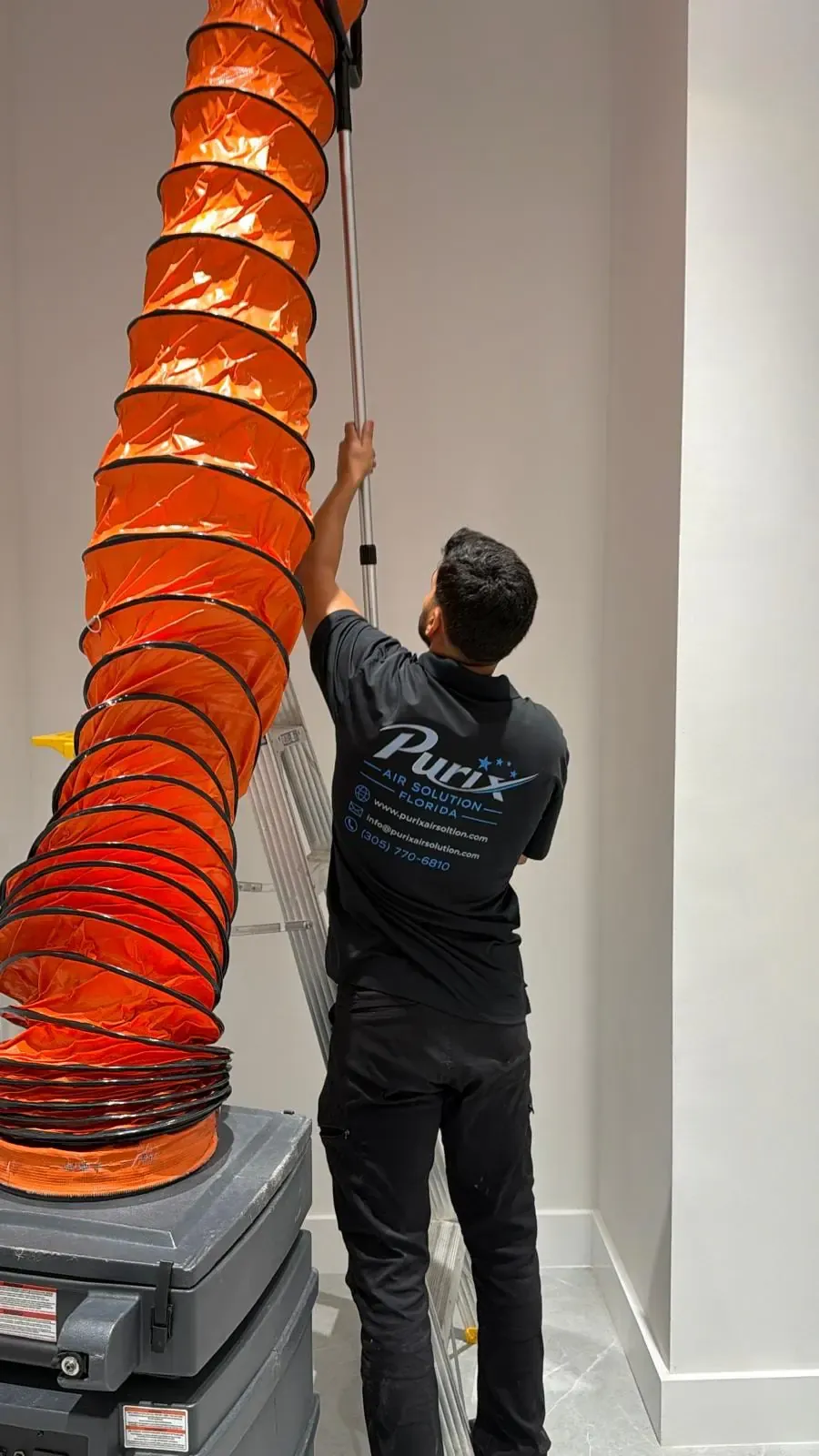 Purix technician running a negative-air hose up to a ceiling duct